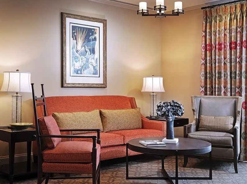 A cozy living room featuring an orange sofa, a gray armchair, a round coffee table, and decorative artwork.