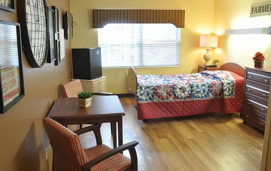 A cozy bedroom with a bed, table, and chairs by a window.