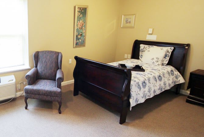 A cozy bedroom with a dark wood bed and an upholstered chair.