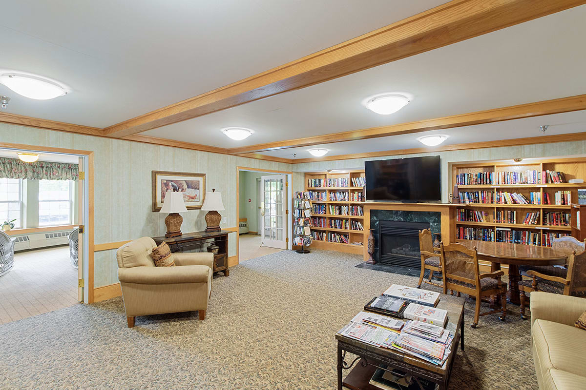 A cozy library room with bookshelves, a seating area, fireplace, and television.