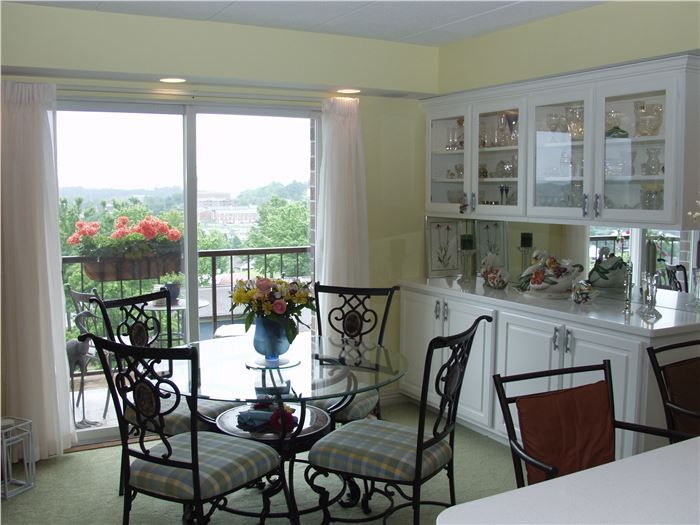 A cozy dining room with a glass table and metal chairs, featuring a scenic view through large windows.