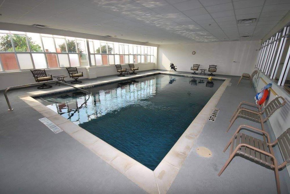 An indoor swimming pool surrounded by chairs and large windows.