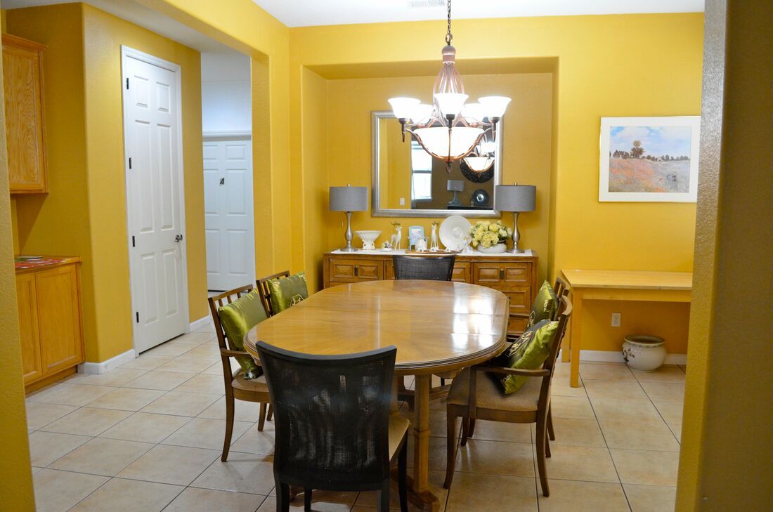 A brightly lit dining room with a wooden table and chairs, featuring yellow walls and a chandelier.