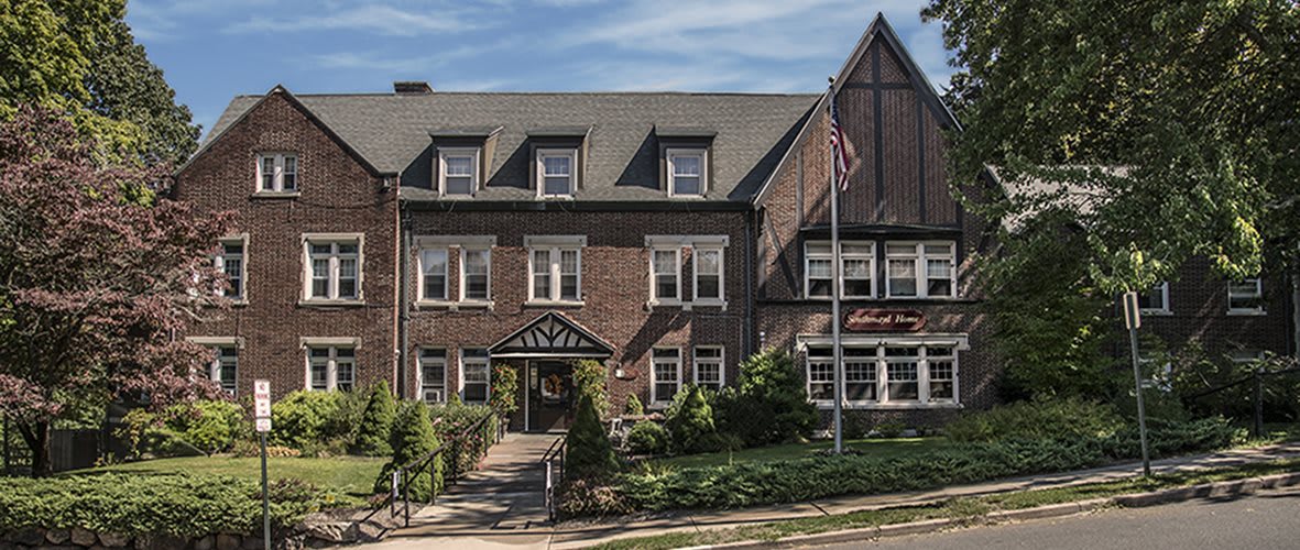A historic brick building with traditional architecture surrounded by greenery, featuring a flagpole with an American flag.