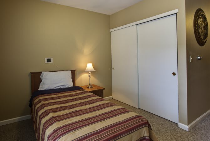A minimalist bedroom with a single bed, nightstand, and a closet.