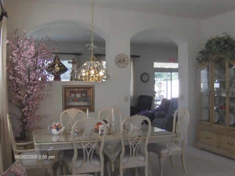 A well-decorated dining room featuring a chandelier, table, and chairs, visible through an archway.