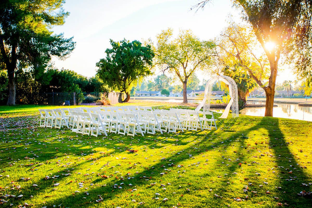 An outdoor wedding setup with rows of white chairs and a ceremonial arch under the trees.