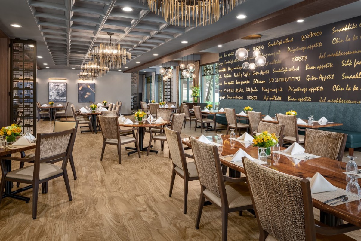 A stylish restaurant interior featuring elegant tables and chairs, decorative lighting, and a chalkboard wall with menu items.