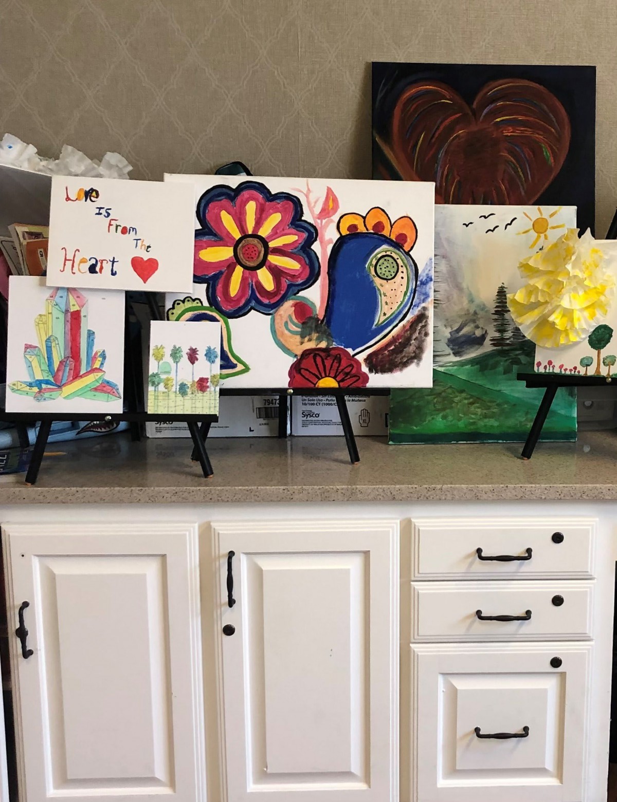 A collection of colorful artwork displayed on small easels atop a cabinet.
