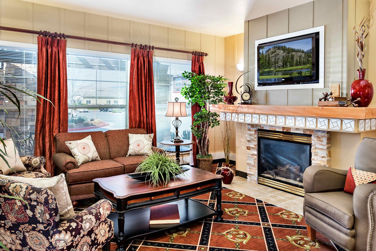 A cozy living room with a fireplace, comfortable seating, and a TV mounted above the mantel.