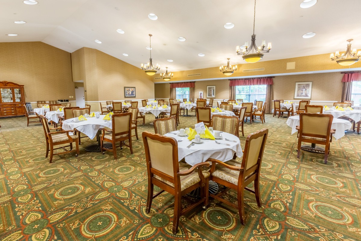 A spacious dining room with neatly set tables and elegant chandeliers.