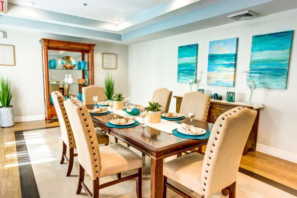 A stylish dining room with a wooden table and upholstered chairs, complemented by nautical-themed artwork.