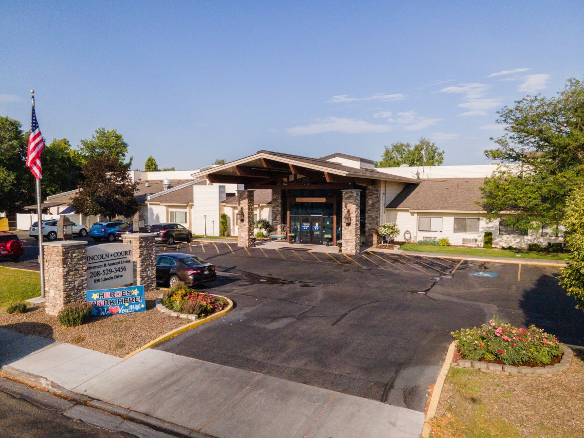 A view of the entrance to a single-story building with a covered driveway and landscaped surroundings under a clear blue sky.