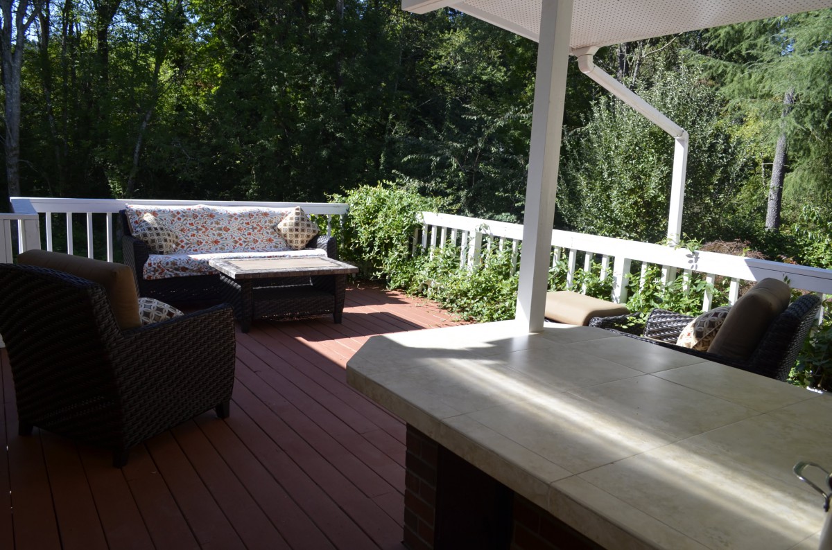 A sunny outdoor deck with comfortable seating and lush greenery.