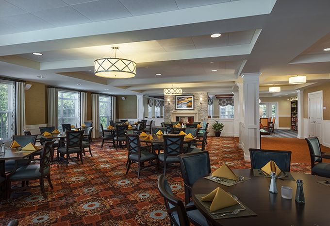 A spacious and elegantly decorated dining room with neatly arranged tables and chairs, featuring warm lighting and a patterned carpet.