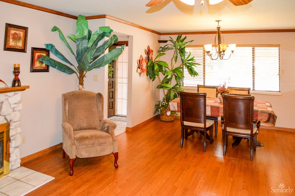 A cozy dining room with wooden flooring, featuring a table, chairs, and indoor plants for decoration.