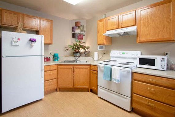 A modern kitchen with wooden cabinets, featuring a refrigerator, oven, and microwave.