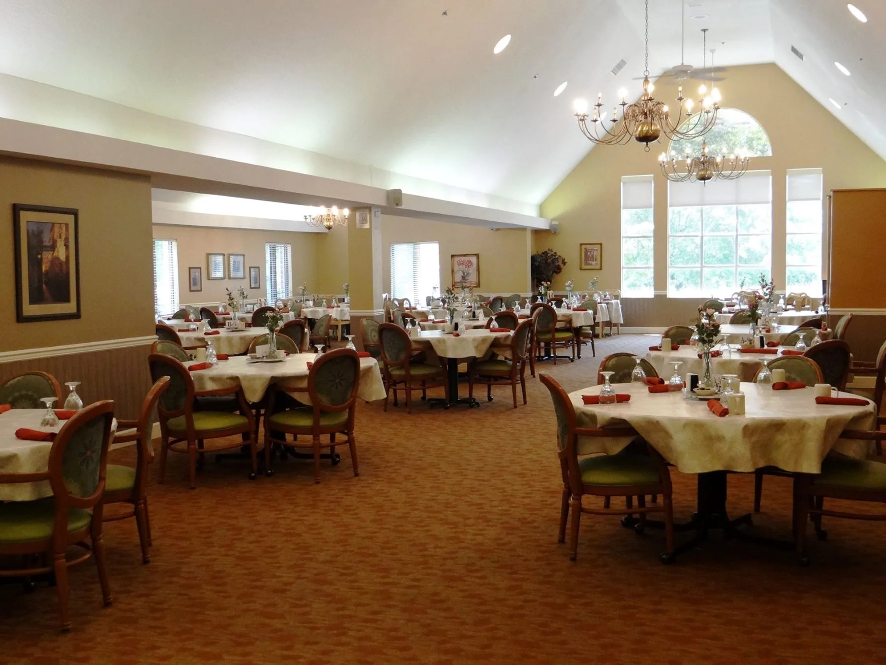 A spacious and elegant dining room with neatly arranged tables and chairs, featuring large windows and chandeliers.