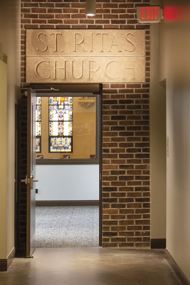 A glimpse through a brick-walled doorway reveals stained glass windows inside a church.