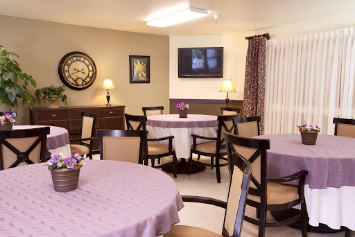 A cozy dining room setup with round tables, comfortable chairs, and a television on the wall.