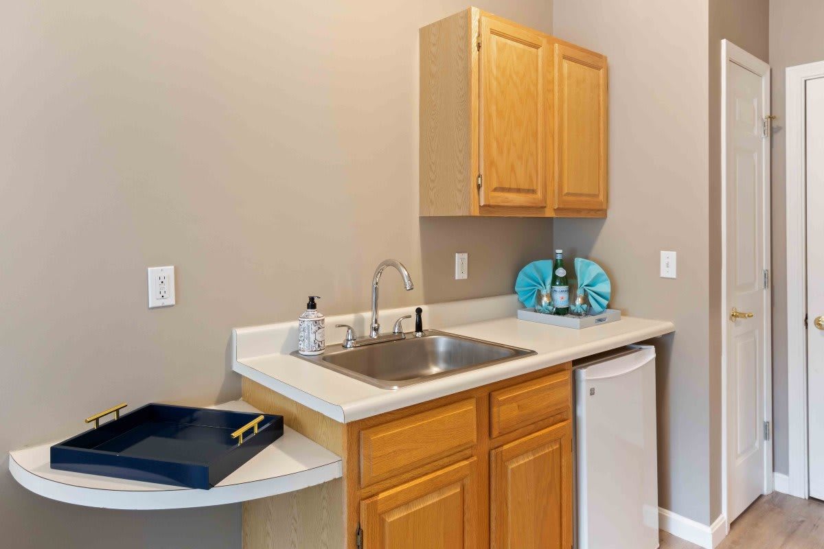 A small kitchenette with a sink, wooden cabinets, and a mini fridge.