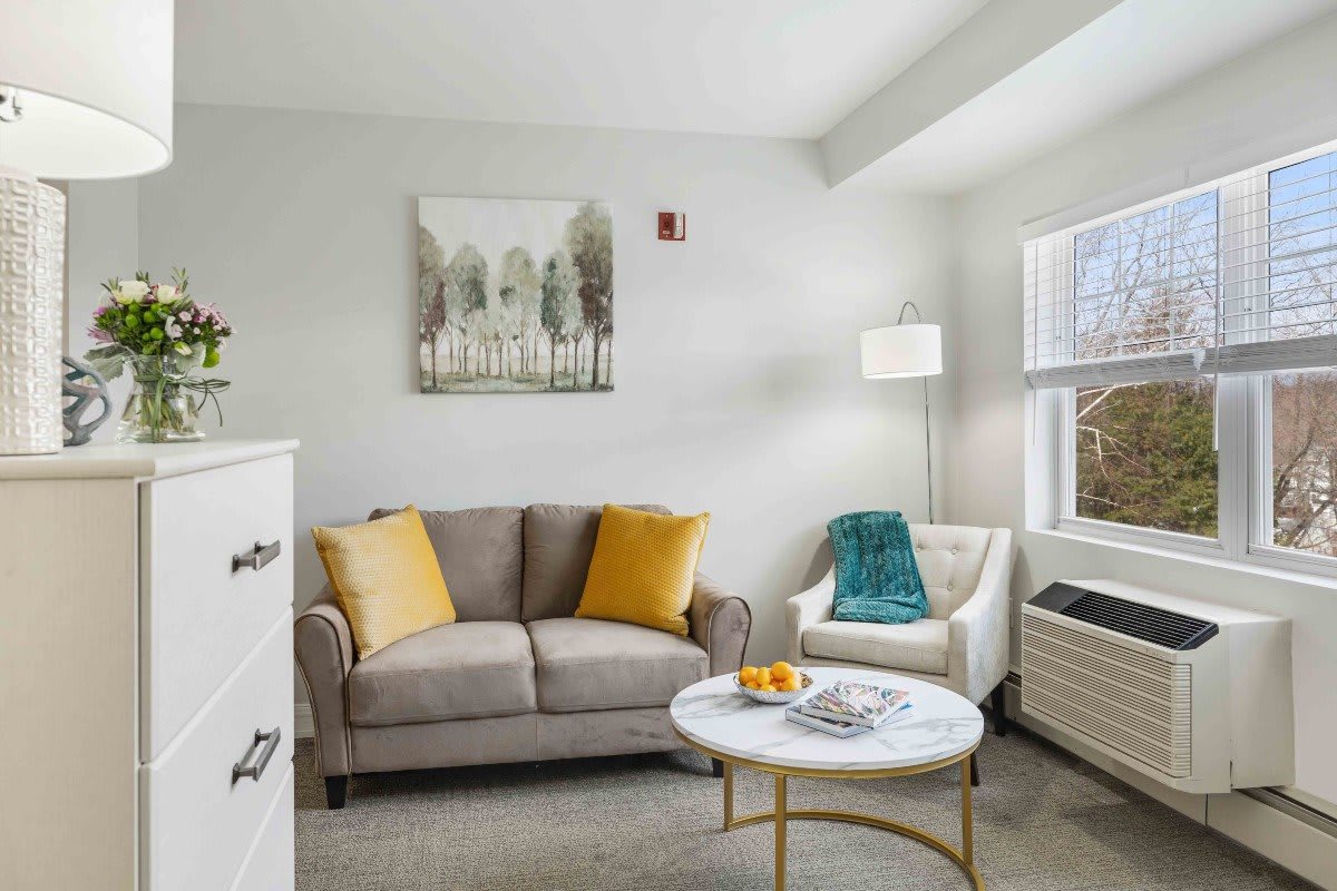 A cozy living room with a gray sofa, accented with yellow pillows, and a white armchair beside a modern coffee table.