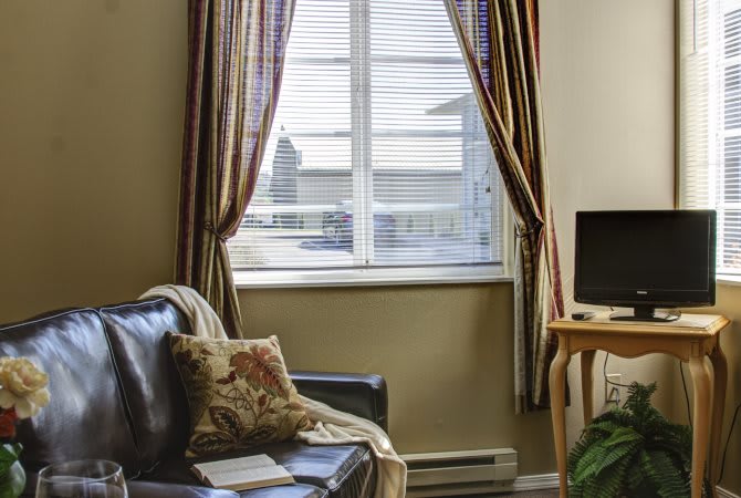 A cozy living room with a sofa and television, featuring a window with striped curtains.