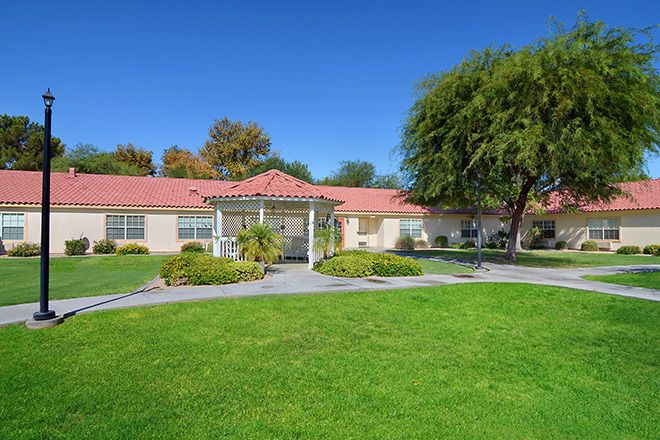 A residential house with a well-maintained lawn and trees under a clear blue sky.