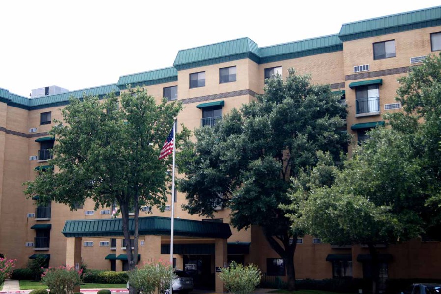 A multi-story building with green accents, surrounded by trees and featuring a flagpole in front.