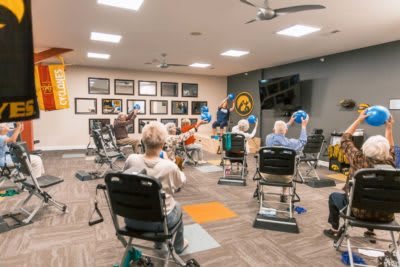 A group of elderly individuals participating in a seated exercise class indoors.