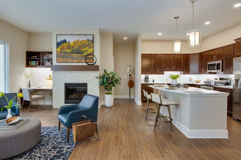 A modern open-concept living room and kitchen area featuring a cozy fireplace, stylish furnishings, and hardwood flooring.