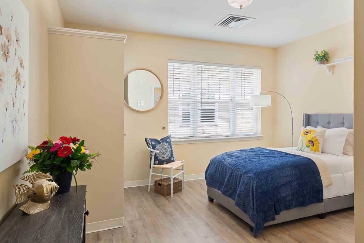 A modern bedroom with a blue bedspread, wooden floor, and decorative elements like a mirror and flowers.