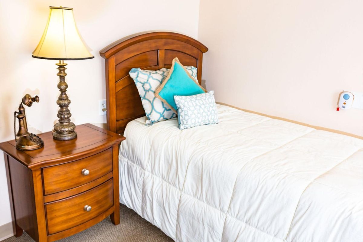 A cozy bedroom with a neatly made bed, colorful pillows, and a wooden nightstand with a lamp.