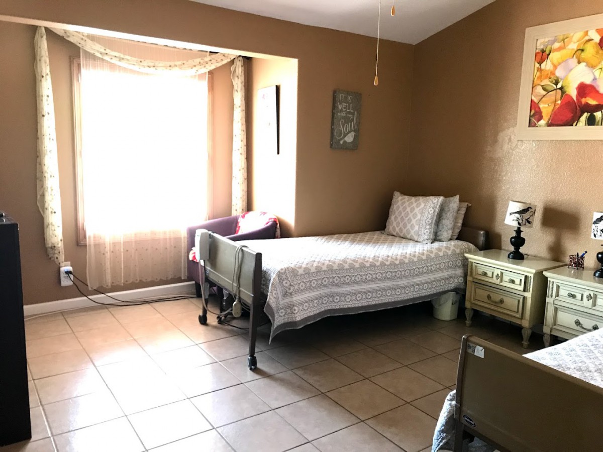 A bright bedroom with a single bed, a chair by the window, and a nightstand with a lamp.