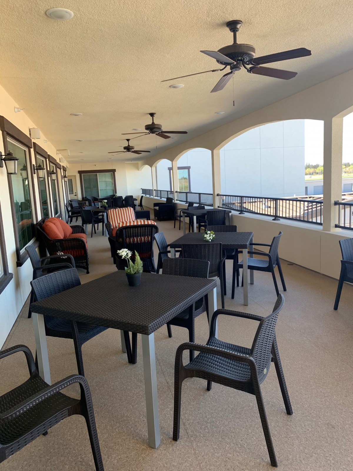 A spacious outdoor patio with tables and chairs arranged under a covered area, complete with ceiling fans for comfort.