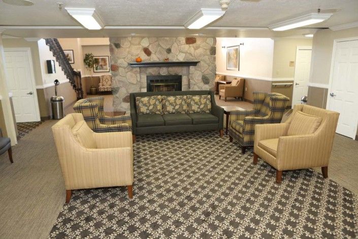 A cozy living room with various sofas and chairs around a stone fireplace, featuring patterned carpet.