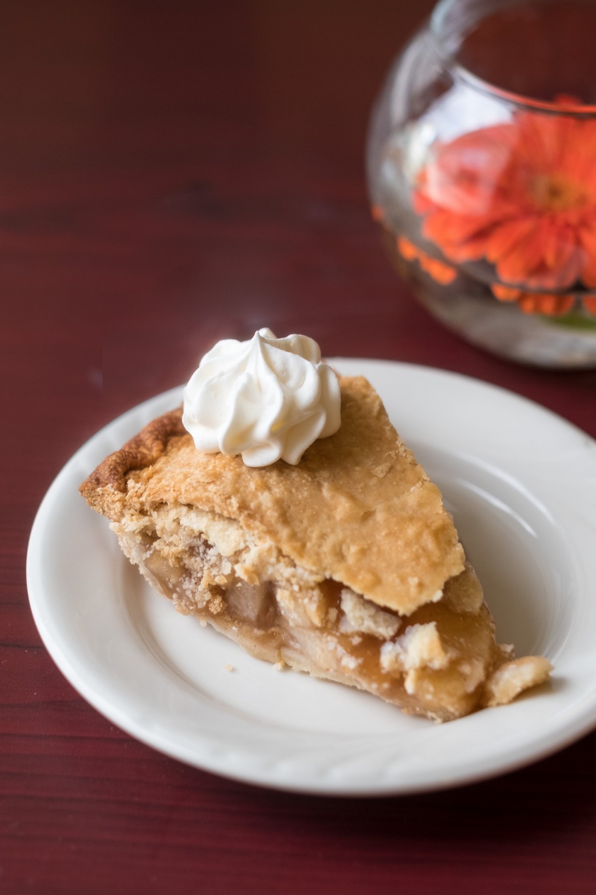 A slice of apple pie topped with whipped cream on a white plate.