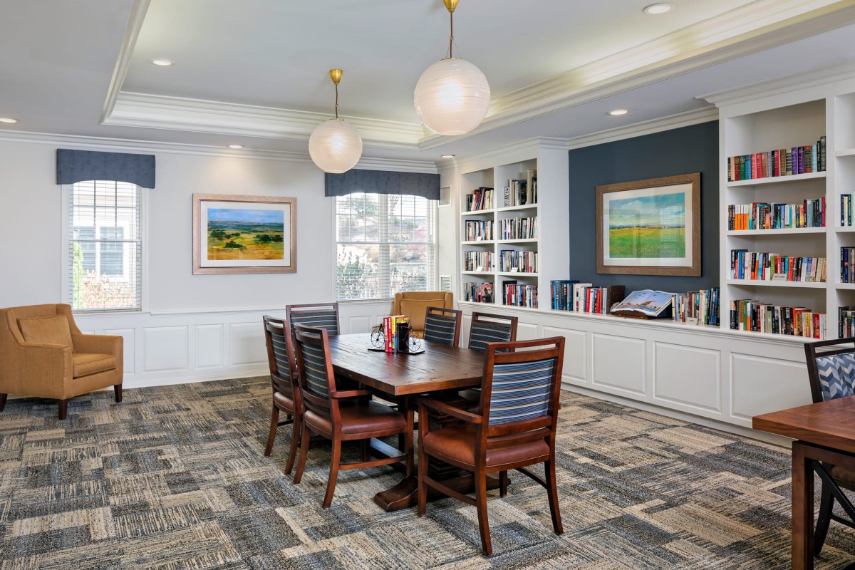 A well-furnished library or conference room featuring a table with chairs, bookshelves, and artwork on the walls.