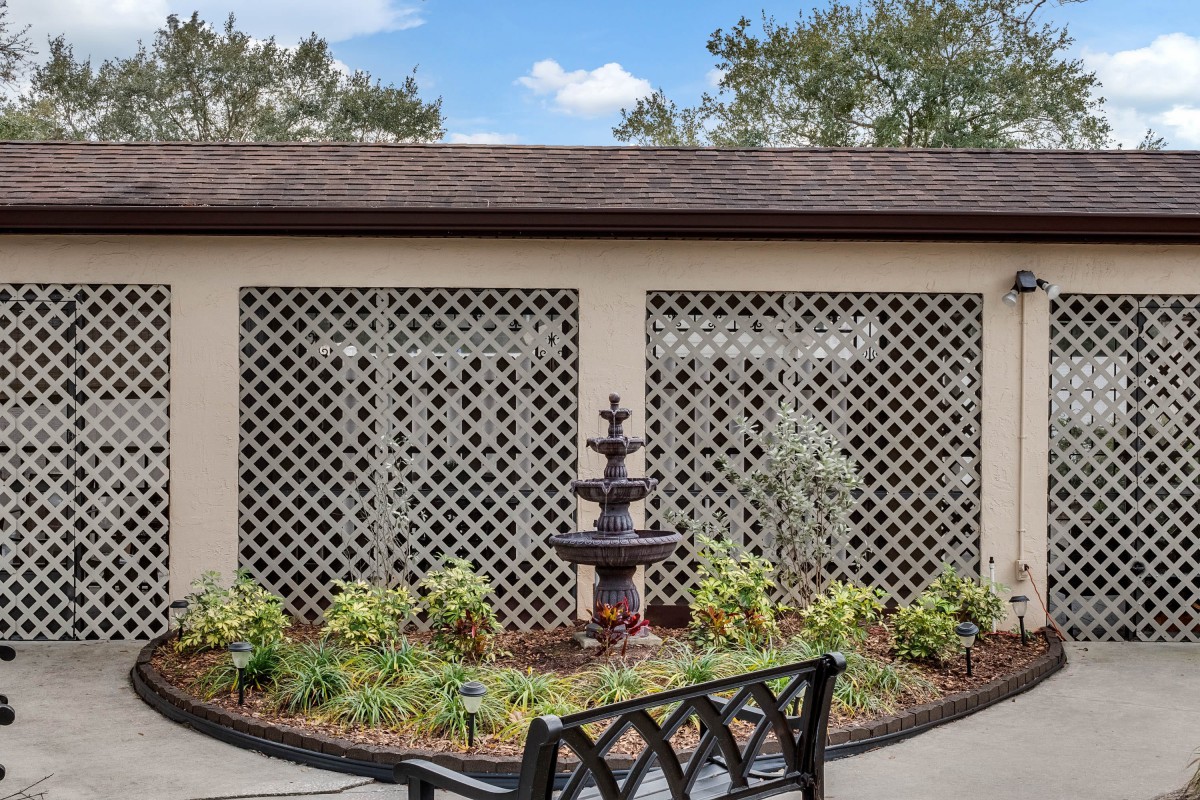 A tranquil garden area featuring a tiered fountain, surrounded by greenery and lattice panels.