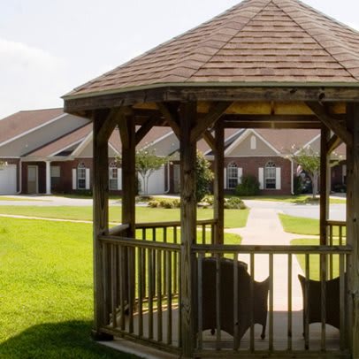 A wooden gazebo on a well-maintained lawn with residential houses in the background.