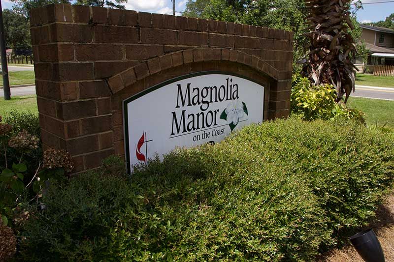 Sign for Magnolia Manor on a brick wall surrounded by greenery.