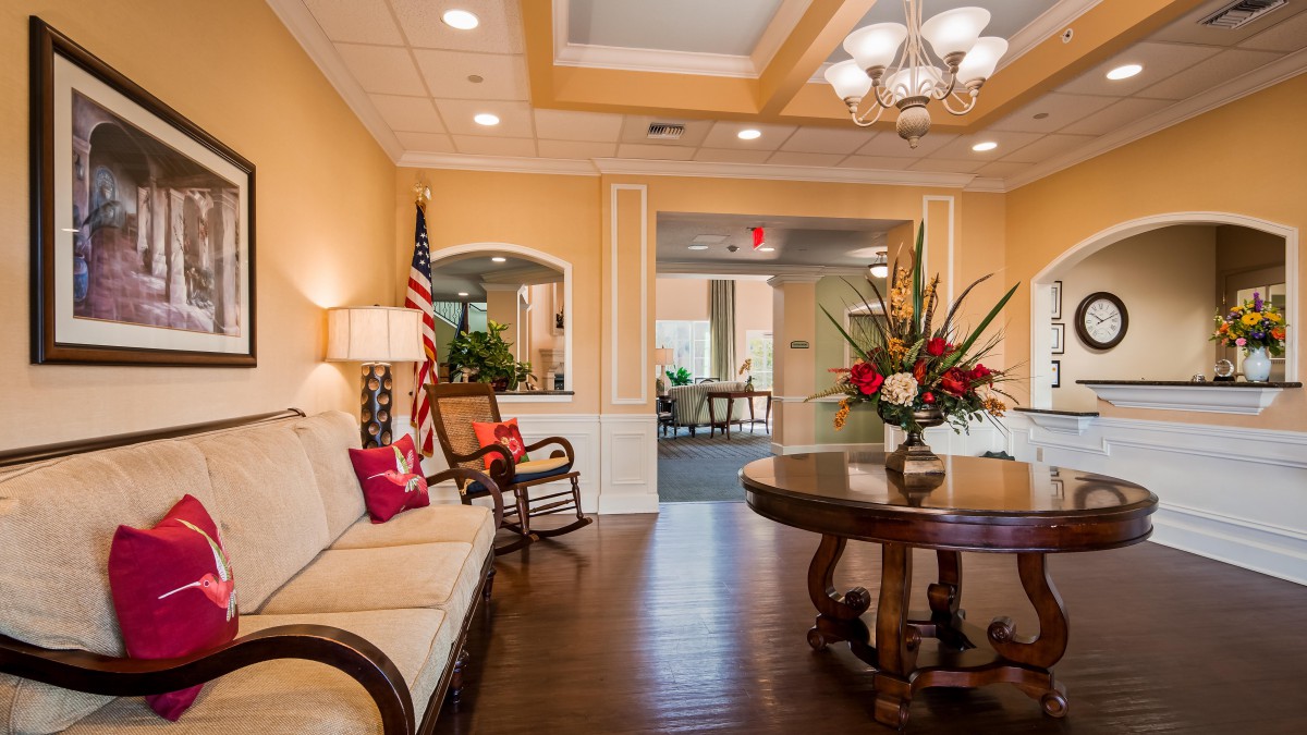A well-decorated lobby area featuring a sofa, round wooden table with floral arrangements, and an American flag.