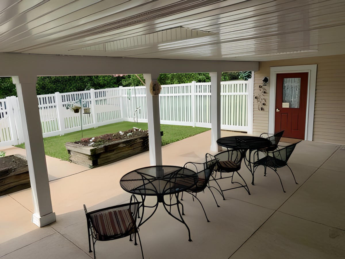A covered outdoor patio with tables and chairs next to a fenced area.