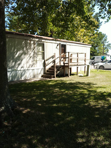 A mobile home with steps leading up to the entrance, surrounded by grass and trees.