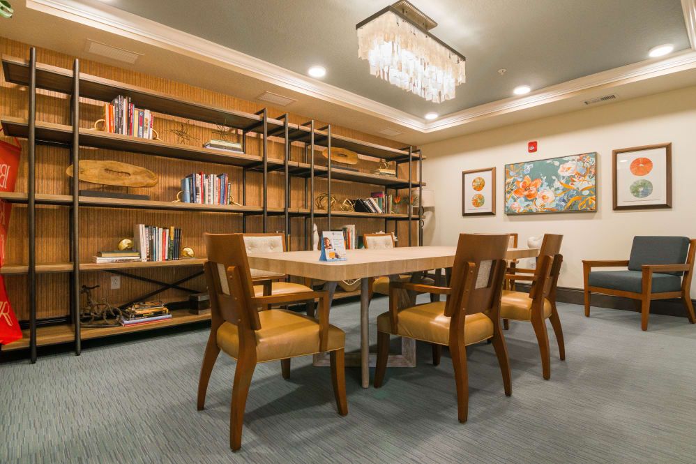 A cozy library setting with a wooden table, chairs, bookshelves, and artwork on the walls.