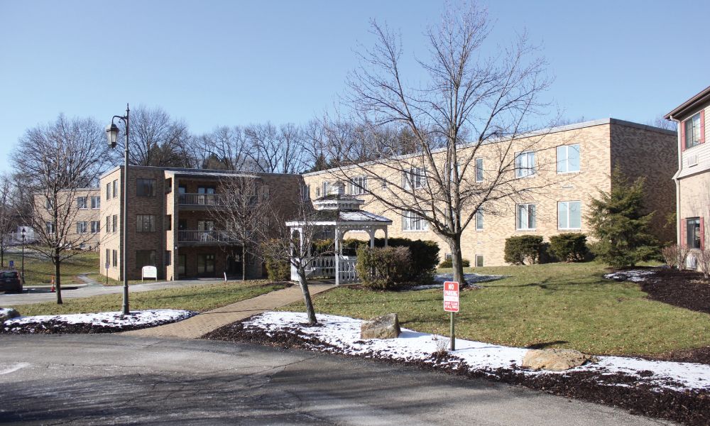 A residential apartment building surrounded by trees with patches of snow on the ground.