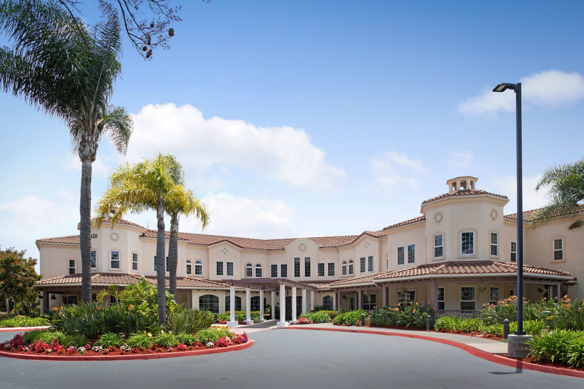 A modern residential building with palm trees and a landscaped driveway.