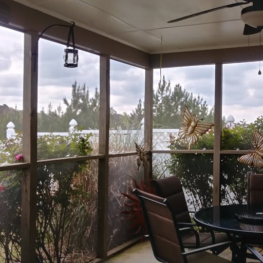 A cozy screened-in porch with patio furniture and plants, offering a view of the outdoors.