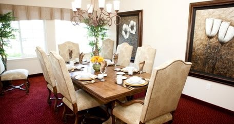 A beautifully arranged dining room with an elegant table setting, featuring a wooden table, upholstered chairs, and a chandelier.