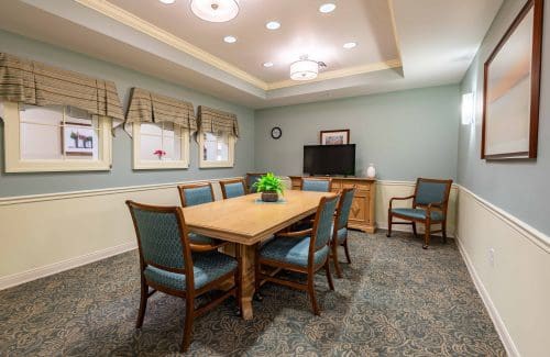 A neatly arranged dining or meeting room with a wooden table, surrounded by upholstered chairs and soft lighting.